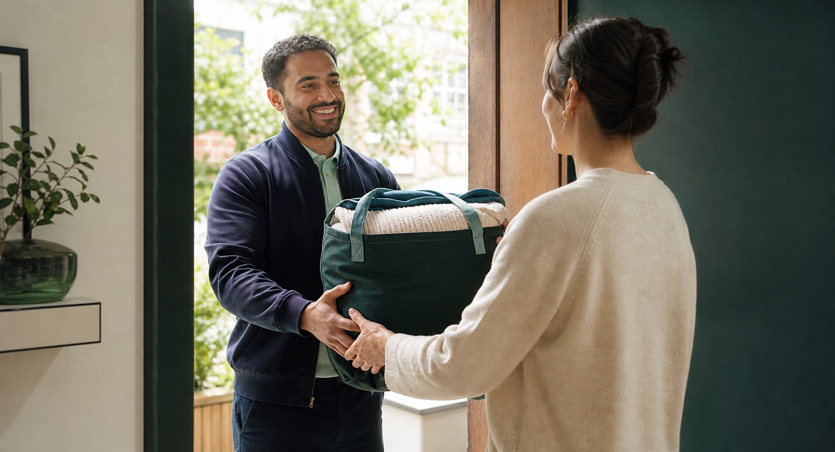 A courier returning a reusable bag of clean folded laundry at a customer's doorway